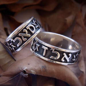 May include: Two silver rings with Hebrew lettering. The rings are on a brown background.