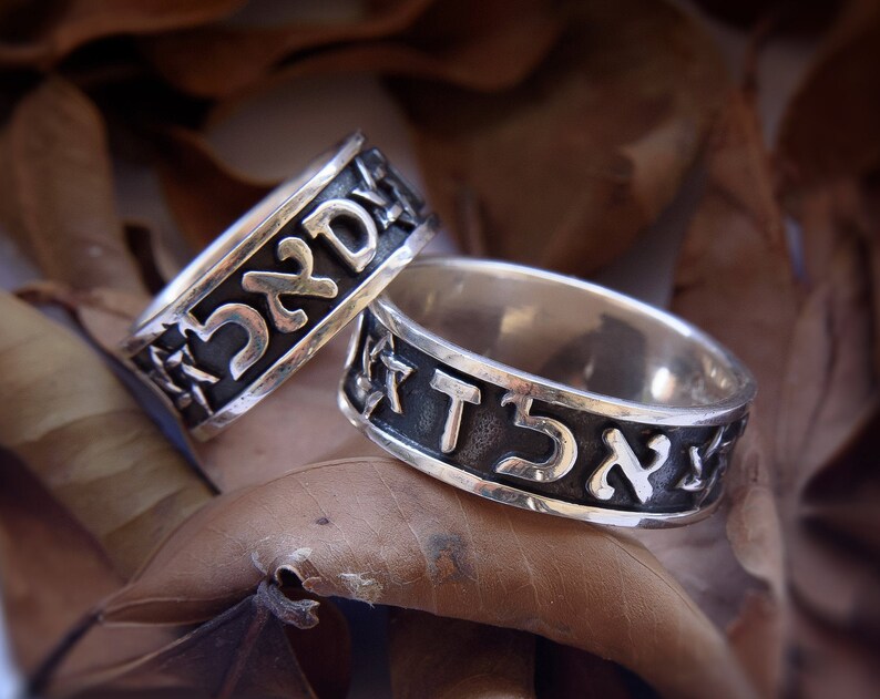 May include: Two silver rings with Hebrew lettering. The rings are on a brown background.