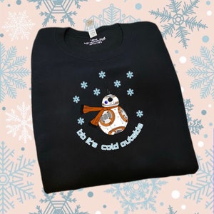 Puede incluir: Sudadera negra con un dibujo animado blanco y naranja de BB-8 de Star Wars con una bufanda y el texto "bb it's cold outside".