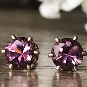 May include: A pair of silver stud earrings with round, faceted, purple gemstones.
