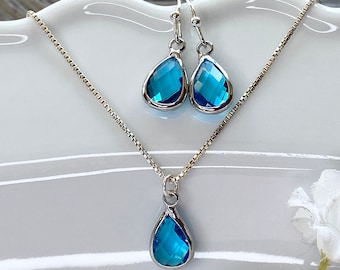 May include: A silver necklace and matching earrings with teardrop-shaped blue crystal pendants.