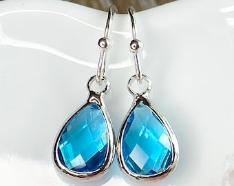 May include: A pair of silver teardrop earrings with light blue crystal stones.