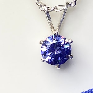 Puede incluir: Un collar de cadena de plata con un colgante redondo de piedra preciosa p&uacute;rpura facetada.