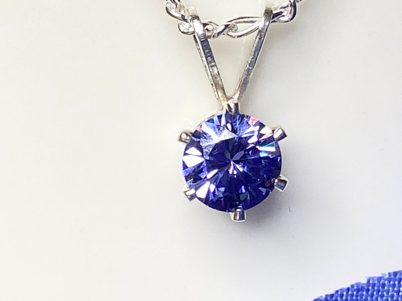 Puede incluir: Un collar de cadena de plata con un colgante redondo de piedra preciosa p&uacute;rpura facetada.