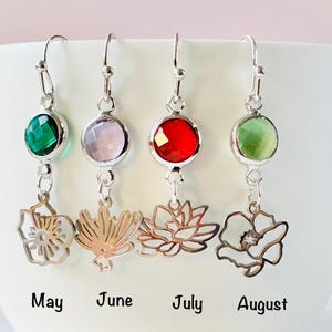 May include: Four silver-toned drop earrings with faceted circular stones in emerald green, light purple, bright red, and pale green. Each earring features a dangling open-work metal flower charm. Text below reads May, June, July, and August.