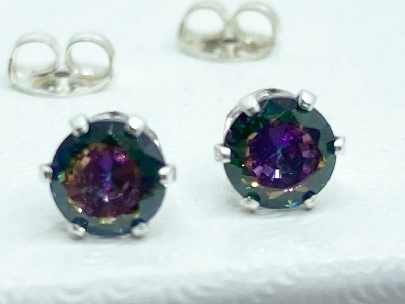 Puede incluir: Un par de pendientes de plata con piedras preciosas redondas e iridiscentes. Las piedras preciosas tienen un color morado oscuro, verde y azul.