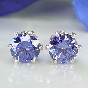 Puede incluir: Un par de pendientes de plata con una piedra preciosa redonda y facetada de color morado en cada pendiente.