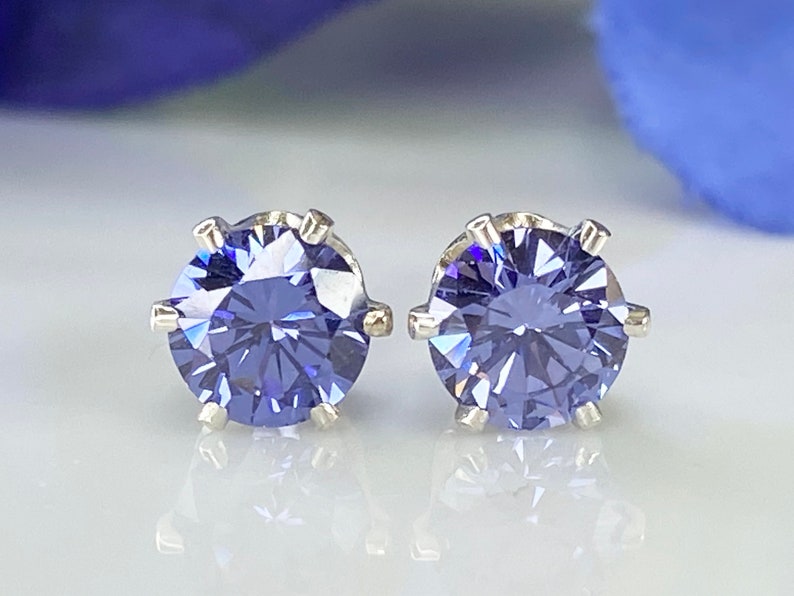 Puede incluir: Un par de pendientes de plata con una piedra preciosa redonda y facetada de color morado en cada pendiente.