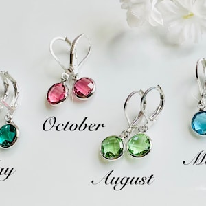 May include: Four pairs of silver leverback earrings with colorful gemstone drops. The earrings are labeled "May", "October", "August", and "March". The gemstones are green, pink, light green, and blue. White flowers are in the background.