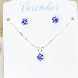 Puede incluir: Un conjunto de collar y pendientes de plata con una piedra preciosa azul. La tarjeta dice "Diciembre, Leal, Honesto, Ambicioso".