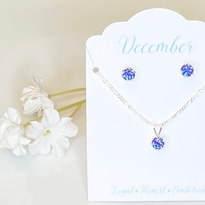 Puede incluir: Un conjunto de collar y pendientes de plata con un colgante de piedra preciosa azul y pendientes a juego. La tarjeta dice "Diciembre" y "Leal, honesto, ambicioso".