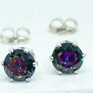 Puede incluir: Un par de pendientes de plata con piedras preciosas redondas e iridiscentes. Las piedras preciosas tienen una base verde oscuro con destellos de morado, azul y rojo.