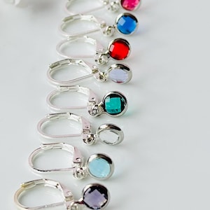May include: A collection of leverback earrings with colorful, faceted gemstones. The earrings feature silver-toned metal and a variety of jewel tones, including blue, yellow, pink, red, green, and purple. The gemstones are approximately 0.25 inches in diameter.