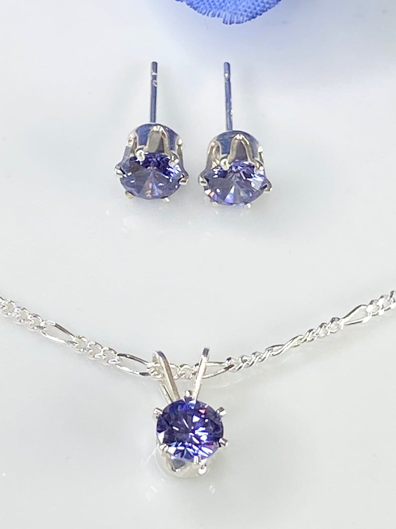 Puede incluir: Un collar de plata con un colgante que presenta una piedra preciosa p&uacute;rpura. El collar se combina con un juego de pendientes de bot&oacute;n a juego con piedras preciosas p&uacute;rpuras.