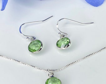 May include: A silver necklace and earrings set with green gemstone pendants. The necklace has a delicate chain and the earrings have simple hooks.