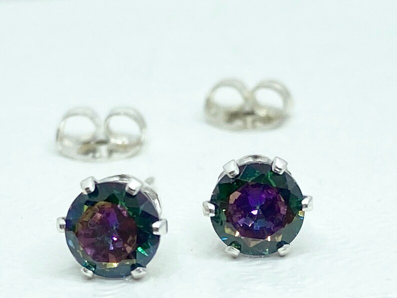 Puede incluir: Un par de pendientes de plata con una piedra preciosa redonda e iridiscente en el centro. La piedra preciosa presenta un arco&iacute;ris de colores, incluyendo morado, verde y azul.
