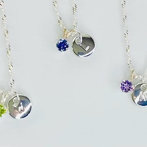 Può includere: Tre collane a catena ritorta color argento, ciascuna con un piccolo ciondolo circolare inciso con una lettera e una pietra preziosa sfaccettata. Sono visibili le lettere W, L e N, abbinate a pietre color verde lime, blu e viola.