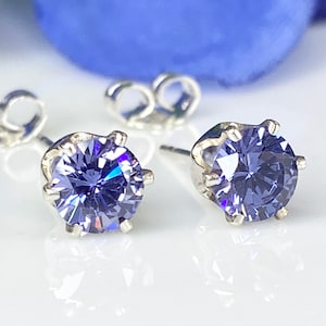 Puede incluir: Un par de pendientes de plata con una piedra redonda de color p&uacute;rpura en cada pendiente.