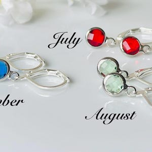 May include: Silver leverback earrings with round, faceted gemstones in blue, red, and green. The word "July", "August", and "September" are written in cursive. The earrings are displayed on a white surface.