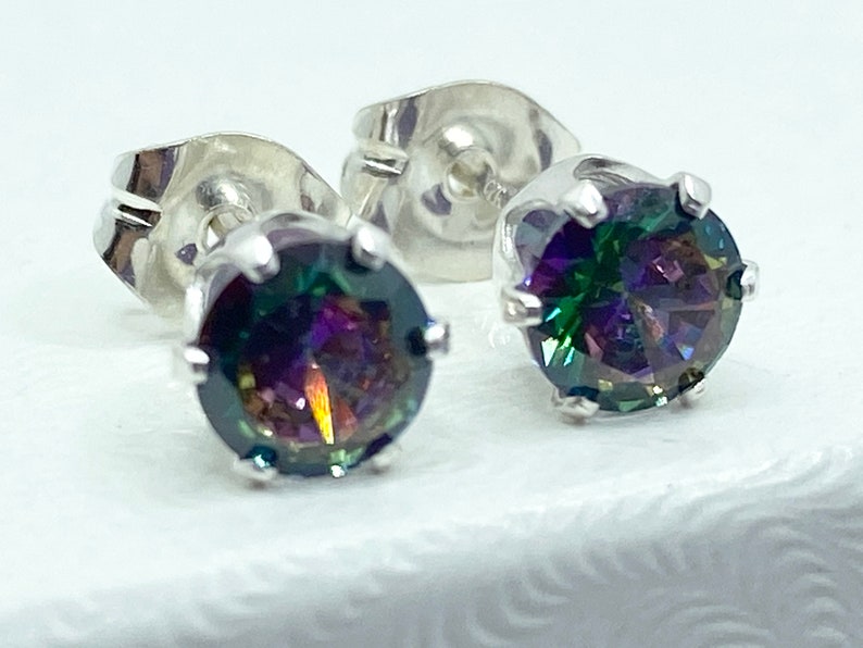 Puede incluir: Un par de pendientes de plata con piedras redondas iridiscentes. Las piedras preciosas presentan un arco&iacute;ris de colores, incluyendo verde, azul, morado y rojo.