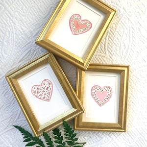 May include: A white ceramic mug with a black handle and the text "But First, Coffee" in a bold, black font. The mug is set against a blurred background, suggesting a cozy setting.