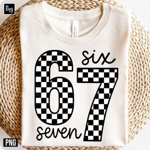 K&ouml;nnte beinhalten: Cremefarbenes T-Shirt mit den Zahlen "67" in einem schwarz-wei&szlig;en Schachbrettmuster. Das Wort "six" steht &uuml;ber der Zahl 6 und das Wort "seven" unter der Zahl 7. Das Shirt ist aus weichem Material.