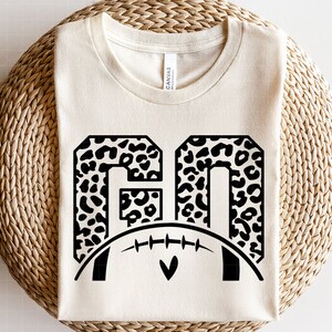 May include: A white t-shirt with a black and white leopard print design of the numbers "60" with a football underneath.