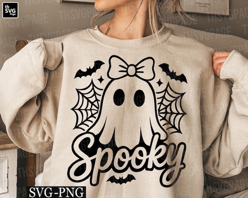 May include: Beige sweatshirt with a black graphic of a ghost wearing a bow, spiderwebs, bats, and the word "Spooky". The design is perfect for Halloween and fall. The sweatshirt is made of a soft material.