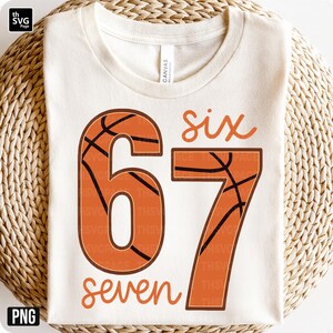 May include: Cream-colored t-shirt with the numbers "67" in orange, designed to resemble basketballs. The word "six" is above the "6" and "seven" is below the "7". The shirt is made of a soft material.