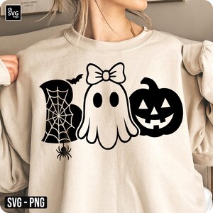 May include: Beige sweatshirt with a black Halloween-themed graphic. The graphic includes the word "BOO" with a spider web, a ghost with a bow, a bat, a spider, and a jack-o'-lantern. The design is in a simple, clean style.