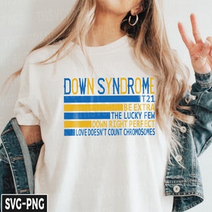 Pode incluir: Camiseta branca com listras azuis e amarelas e o texto "DOWN SYNDROME T21 BE EXTRA THE LUCKY FEW DOWN RIGHT PERFECT LOVE DOESN'T COUNT CHROMOSOMES".