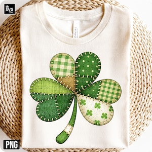 May include: Cream-colored t-shirt featuring a large, patchwork shamrock design. The shamrock is composed of various green patterns, including polka dots, gingham, and solid fabrics, stitched together with visible thread. A festive St. Patrick's Day theme.