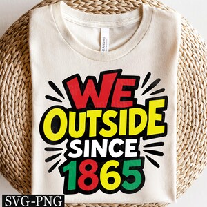 Könnte beinhalten: Cremefarbenes T-Shirt mit dem Schriftzug "WE OUTSIDE SINCE 1865" in fetter, farbenfroher Schrift. Der Text ist schwarz umrandet und mit roten, gelben und grünen Akzenten versehen. Das Shirt wird auf einer gewebten, kreisförmigen Oberfläche präsentiert.