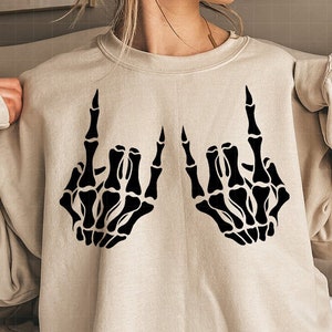 May include: A beige sweatshirt with a black skeleton hand design making the rock and roll hand gesture.