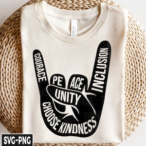 May include: A white t-shirt with a black hand symbol design. The hand is making a rock and roll sign. The words "Courage", "Peace", "Unity", "Choose", "Kindness", and "Inclusion" are written around the hand.