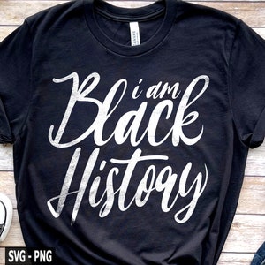 May include: Black t-shirt with the text "I am Black History" in a white, cursive font. The shirt is a crew neck style and has rolled-up sleeves. The image also includes a pair of sneakers and a portion of denim jeans.