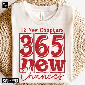 May include: Cream-colored t-shirt with the text "12 New Chapters, 365 New Chances" in red. The numbers are in a bold, blocky font, and the words "New Chances" are in a script font. The shirt is displayed on a woven surface.