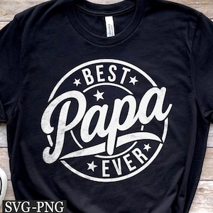以下が含まれることがあります： 「BEST Papa EVER」と書かれた白い円形グラフィックが特徴の黒いTシャツ。デザインには星とバナーが含まれています。シャツは柔らかい素材で作られています。
