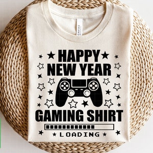 K&ouml;nnte beinhalten: Ein wei&szlig;es T-Shirt mit einem schwarzen Grafikdesign, auf dem "Happy New Year Gaming Shirt" mit einem Videospiel-Controller und einer Ladeanzeige steht.