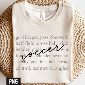 May include: A beige t-shirt with the word "soccer" written in black cursive script. The text is surrounded by a list of soccer terms, including "goal keeper", "pass", "footwork", "half field", "cross ball", "kick", "header", "goal", "win", "free kick", "defender", "sweeper", "penalty", "goal line", "breakaway", "control", "teamwork", and "angles".