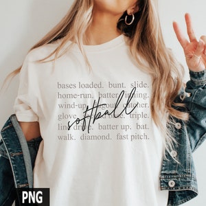 May include: Cream-colored t-shirt with the word "softball" in a cursive font, surrounded by softball-related terms. The shirt is paired with a denim jacket. The image includes the text "bases loaded, bunt, slide, home-run, batter, inning, wind-up, dugout, catcher, glove, line drive, batter up, bat, walk, diamond, fast pitch."