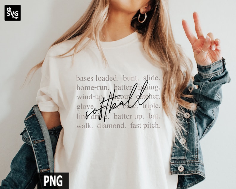 May include: Cream-colored t-shirt with the word "softball" in a cursive font, surrounded by softball-related terms. The shirt is paired with a denim jacket. The image includes the text "bases loaded, bunt, slide, home-run, batter, inning, wind-up, dugout, catcher, glove, line drive, batter up, bat, walk, diamond, fast pitch."