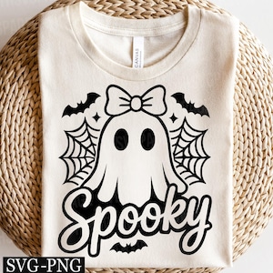 May include: Cream-colored t-shirt featuring a black graphic of a ghost with a bow, spiderwebs, and bats. The word "Spooky" is written in a script font below the ghost. The shirt is made of a soft material.