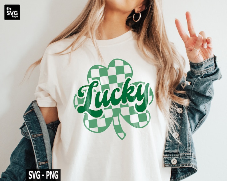 May include: A white t-shirt with a green shamrock design. The shamrock is made up of checkered squares in green and white. The word "Lucky" is written in green cursive letters inside the shamrock.