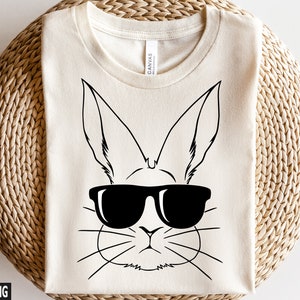 May include: A white t-shirt featuring a black and white illustration of a bunny wearing sunglasses. The bunny has long ears and a cute, cartoon-like face.