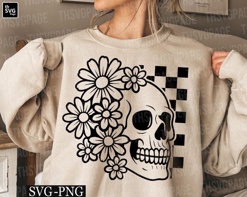 May include: Beige sweatshirt featuring a black and white floral skull design. The skull is on the right side, with a checkerboard pattern behind it. The design includes daisies and the text "SVG-PNG".