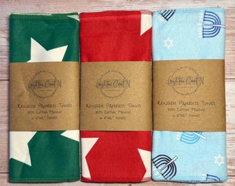 May include: Three reusable paperless towels in green, red, and light blue, each wrapped with a brown paper band. The green towel has white stars, the red has white stars, and the blue has menorahs and stars. Each towel is 10x12 inches.