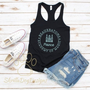 May include: Black tank top with a white circle graphic featuring the text "Beauxbatons Academy of Magic" and a drawing of a building with the word "France" underneath.