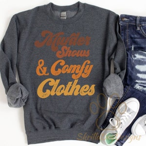 May include: A dark gray sweatshirt with the text "Murder Shows & Comfy Clothes" in a retro, orange and yellow font.