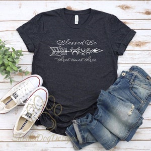 May include: A dark gray t-shirt with a white graphic of an arrow with moons and the text "Blessed Be three times three".
